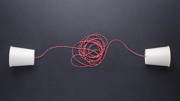Das Bild zeigt zwei weiße Pappbecher die sich mit einem rotem Faden verbinden.